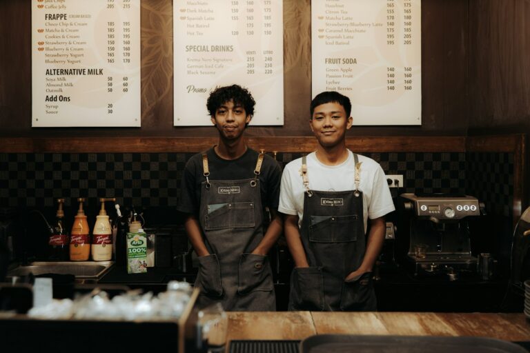 Két fiatal barista kötényben egy kávézó pultja mögött